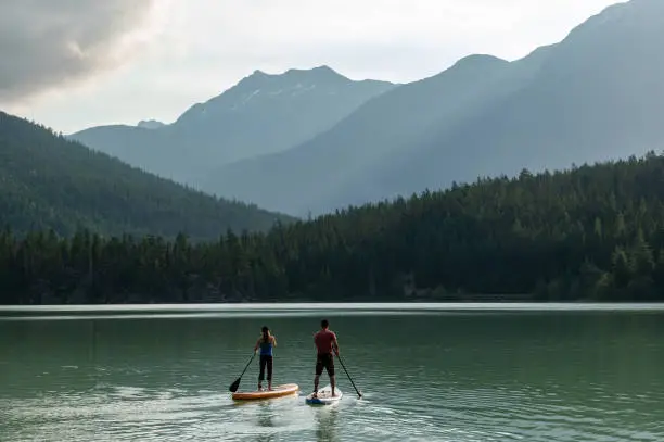 Top travel destinations in Canada. Couple paddleboarding on Green Lake in Whistler, BC. Paddleboard adventure in the mountains.