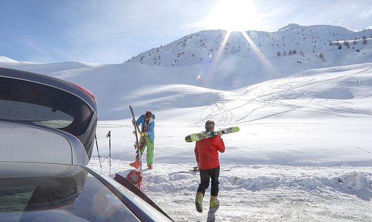 Mother and three teenage kids are walking on a parking lot in in Austrian Alps. They are carrying the skis.\nCanon R5