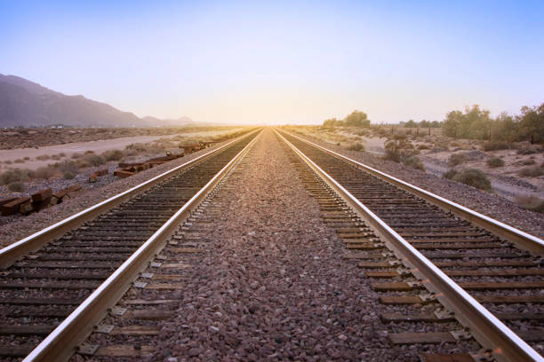 Two parallel rail road tracks vanishing on the horizon line and the golden setting sun stock photo
