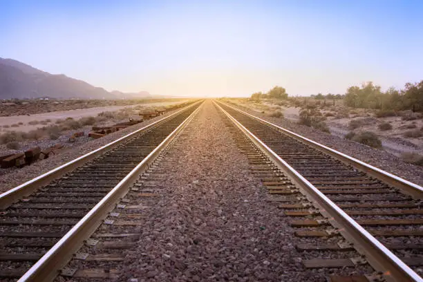 Photo of Two parallel rail road tracks vanishing on the horizon line and the golden setting sun