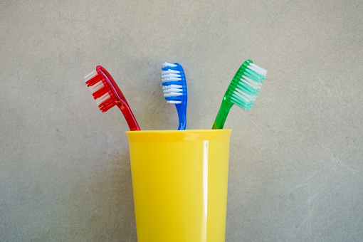 Three toothbrushes consisting of red, blue and green in a yellow plastic cup on a gray wall
