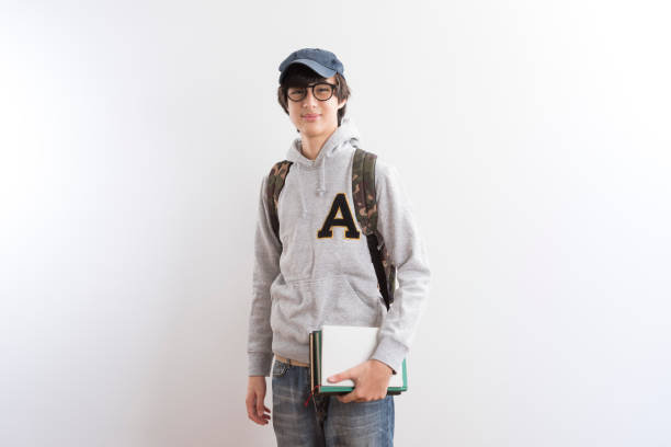 istock Handsome teen boy students carrying a backpack and books standing on white background. 1329301594