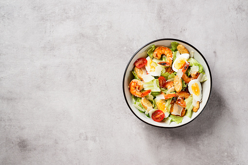 Fresh Shrimp Caesar Salad with parmesan cheese and Croutons. Gray background, top view, space for text.