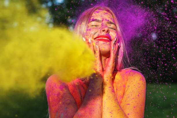 istock Merry blonde woman posing with exploding yellow paint at summer Holi festival 1329307640