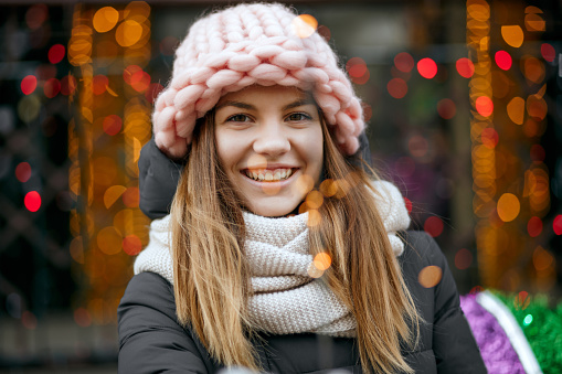 Gorgeous smiling blonde woman wearing winter outfit celebrating Christmas at the garlands blurred background. Empty space