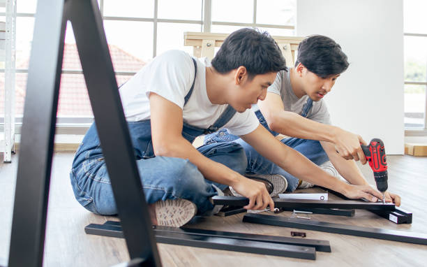 istock Two Asian handsome men wearing blue overalls, helping or supporting each other to assemble make DIY furniture following manual at home. 1329308921