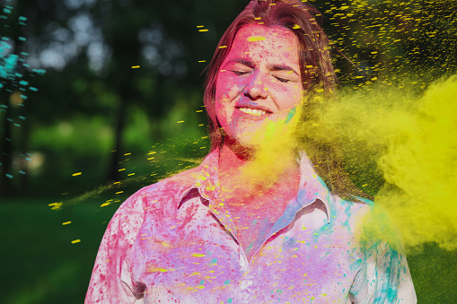 Wonderful smiling brunette woman with short hair posing with exploding yellow Holi paint in the park. Space for text
