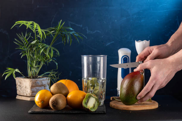 istock Slice the mango for a cocktail. Slice the mango for a smoothie. Make smoothies in a blender. Mango and knife in hand. Blue background. 1329309648