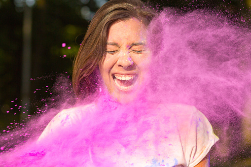 Closeup portrait of expressive brunette asian woman with long hair playing with purple Holi paint