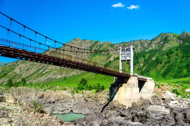 old steel suspension bridge over mountain river