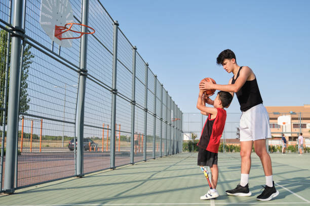 entrenador de baloncesto que muestra cómo disparar baloncesto a un niño con una prótesis de pierna. entrenador entrenando a un niño. - child group of people teenager sibling fotografías e imágenes de stock