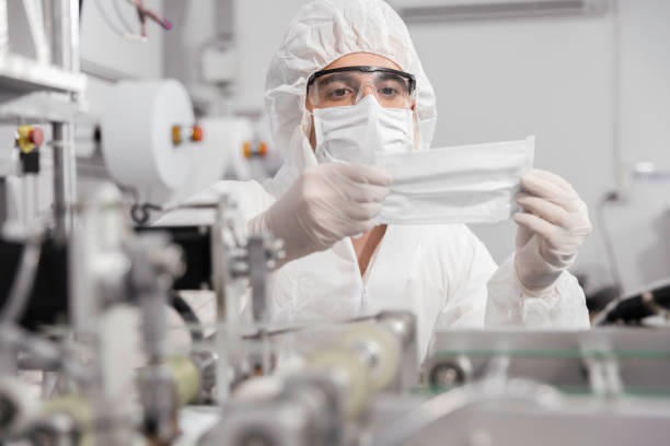 istock Technician or engineer in PPE working checking mask production at clean factory or laboratory, Face mask manufacturing production automation or quality concept 1329318786
