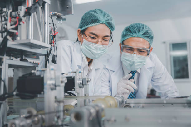 two asian doctor or engineer working at clean medical mask production factory, production hygiene medical manufacturing qaulity inspection concept - equipamento médico imagens e fotografias de stock