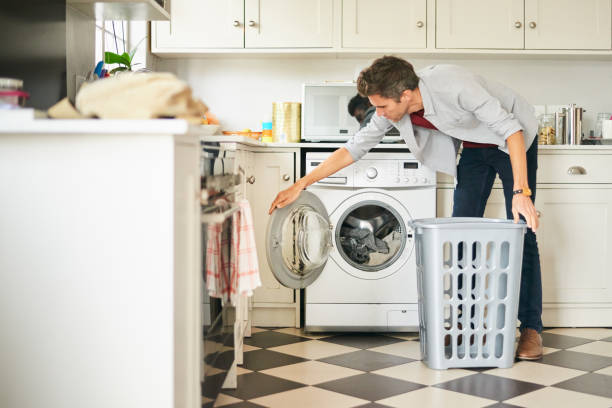 Young man doing laundry in washing machine in his kitchen
