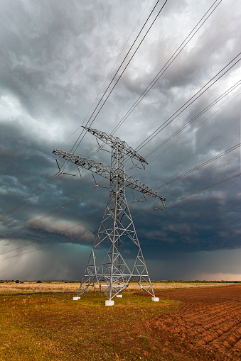 Dangerous severe storm approaches high voltage electricity power lines in agricultural field: steel pylons carrying multiple power cables appear to stand defiant as the maelstrom bears down.
