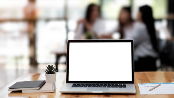 istock Photo of computer laptop with white blank screen putting on the modern working table with business people having a blurred meeting in the background. 1329326794