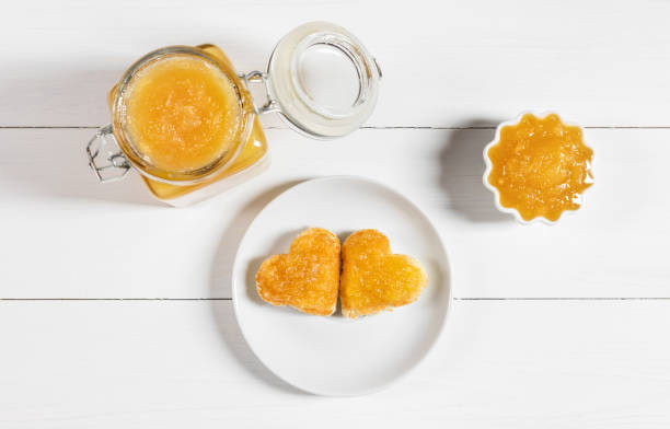 Fruit yellow jam on a white wooden background. Heart shaped delicious toast on a plate. Top view, flat lay. Fruit yellow jam on a white wooden background. Heart shaped delicious toast on a plate. View from above. kaki marmelade stock pictures, royalty-free photos & images