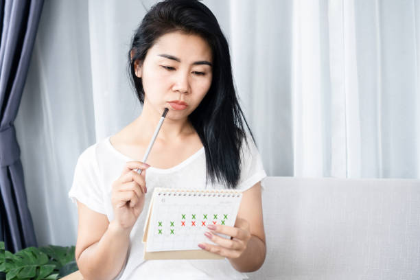 donna asiatica che ha problemi con l'amenorrea, periodi irregolari guardando il calendario e contando i suoi cicli mestruali - menstruation foto e immagini stock