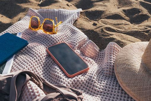 Various beach-related items in an outdoor still life (hat, sandals, swimsuit, beach bag, towel and a mobile phone to stay connected)