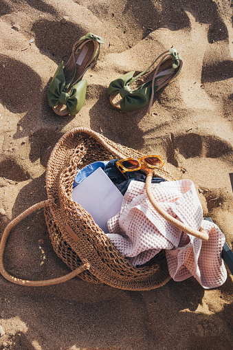 Summer travel essentials: beach paraphernalia in a straw bag on a sandy beach