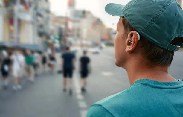 Photo of Human life with a hearing aid. Young man with a hearing aid behind the ear in a noisy city hears people around well