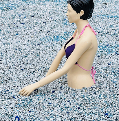 Vintage puppet in bikini sunken in pebbles