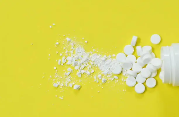 white tablet medicine mashed and  pouring from bottle arranging on yellow background