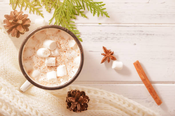 istock hot chocolate mug with marshmallows, cone, cinnamon sticks, white sweater, fir branches on a white wooden background, top view 1329348286