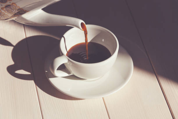 Pouring coffee into coffee cup - summer morning with bright sunlight and shadows