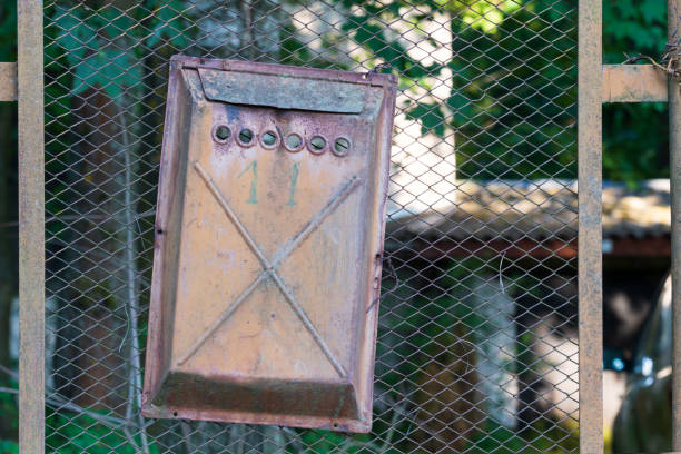 istock An old rusty mailbox hangs crookedly from a wire mesh fence. Several coats of partially peeling paint are visible and number 11. Green vegetation is visible in the background. Background. 1329351366