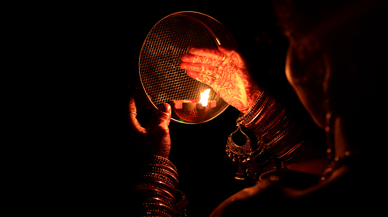 Young Indian woman celebrating Karva Chauth at night. Karva Chauth is a one-day festival celebrated by Hindu women four days after purnima (a full moon) in the month of Kartika. On Karva Chauth women, especially in Northern India, who are married fast from sunrise to moonrise for the safety and longevity of their husbands.