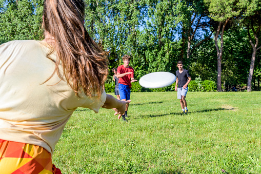 Group of friends have fun play at flying disc in the park in summer time - Girl launches the frisbie at a friends - Sport, education, fun, team, lifestyle concept about healthy life in the outdoor