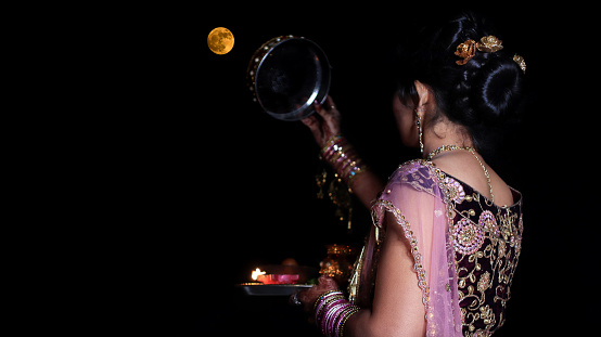 Young woman of Indian ethnicity looking through sieve on Karwa Chauth festival. Karwa Chauth is a festival celebrated by Hindu women from the Indian Subcontinent on the fourth day after Purnima in the month of Kartika. On Karva Chauth women, especially in Northern India, who are married fast from sunrise to moonrise for the safety and longevity of their husbands.