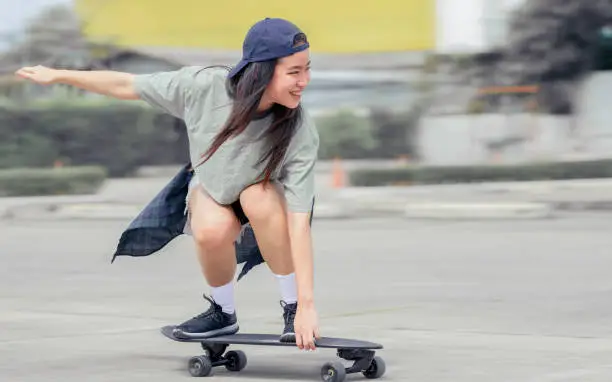 Photo of Beautiful happy Asian healthy woman smiling, motion speed riding and playing extreme sportive skateboard as outdoor activity with happiness, relaxation and fun during holidays in summer vacation.