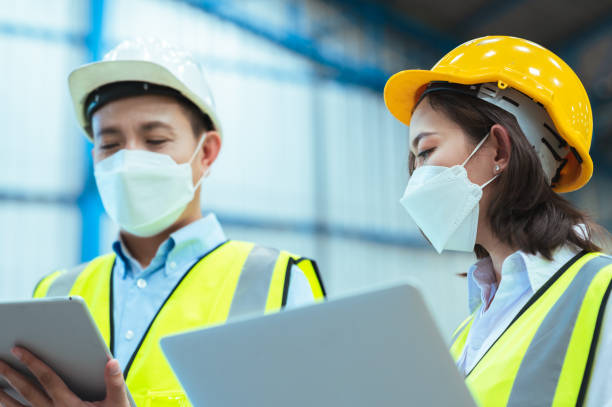 istock Chief industrial engineer inspects the mask factory. Discuss new projects while using a laptop. They showed an assertive attitude. There are employees wearing protective gear working diligently. 1329357656