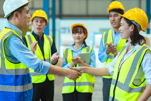 Asian male and female engineers wear protective gear and masks. shake hands to make a deal or celebrate success in the warehouse.