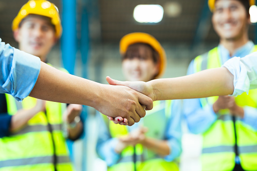 Asian male and female engineers wear protective gear and masks. shake hands to make a deal or celebrate success in the warehouse.