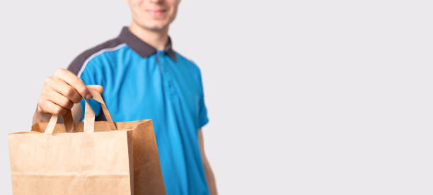 istock Delivery man in a blue polo shirt holding a package carton bag with handless pulling it forward and smiling. 1329360111