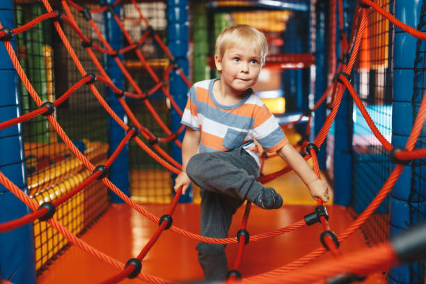 happy boy playing in indoor playground on net trail. child having fun on modern playground. cute kid playing on colorful playground at shopping mall - child jungle gym playground laughing imagens e fotografias de stock