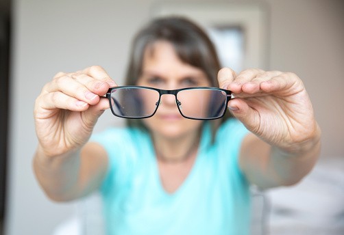 middle aged woman traying to fix her glasses to see better