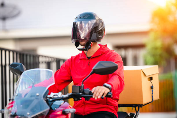 istock Courier in red uniform with a delivery box on back riding a motorcycle check the address to deliver food to the customer. Courier on a motorcycle delivering food in the city. 1329367268