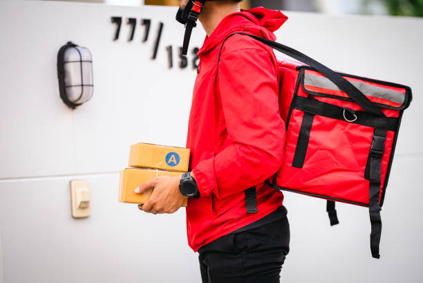 istock Courier in red uniform Delivery man standing with parcels in hands outdoors waiting homeowner open door. Home delivery service and working with service 1329367283
