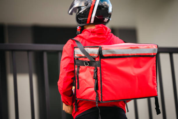 istock Courier in red uniform Delivery man standing with parcels in hands outdoors waiting homeowner open door. Home delivery service and working with service 1329367284