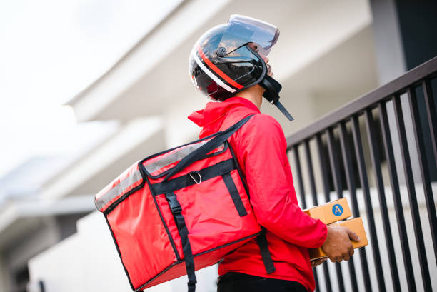 istock Courier in red uniform Delivery man standing with parcels in hands outdoors waiting homeowner open door. Home delivery service and working with service 1329367289