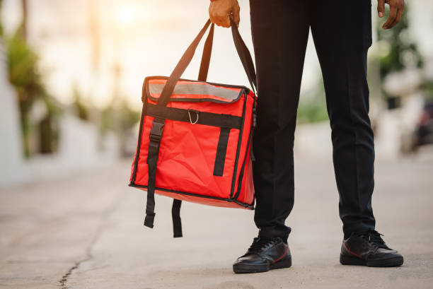 istock Courier in red uniform Delivery man standing with parcels in hands outdoors waiting homeowner open door. Home delivery service and working with service 1329367351