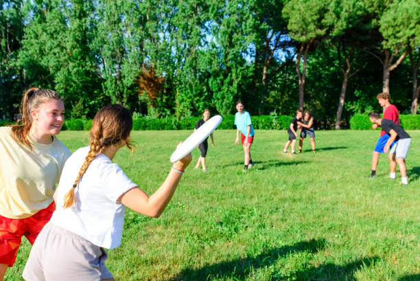 Group of mixed young teenagers people in casual wear playing with flying plastic disk game in a park oudoors. men and women tosses a disc to a teammate in a match. milennial friends outside having fun Group of mixed young teenagers people in casual wear playing with flying plastic disk game in a park oudoors. men and women tosses a disc to a teammate in a match. milennial friends outside having fun plastic disc stock pictures, royalty-free photos & images