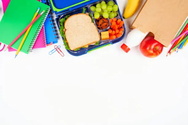 Healthy school lunch with school supplies. Above view top border on a white background. Back to School concept.