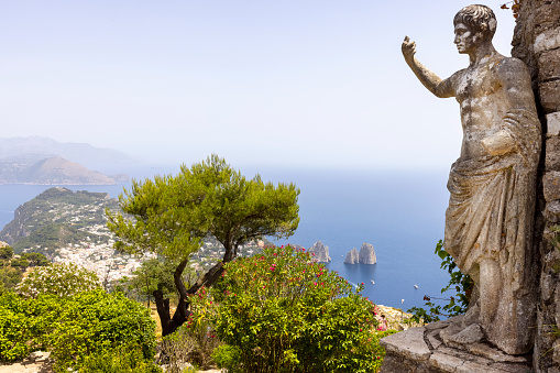 Capri Island; Italy - June 28; 2021: Aerial view from the top of the island Monte Solaro to the Tyrrhenian Sea with rocks Faraglioni; statue of Emperor Augustus in the foreground