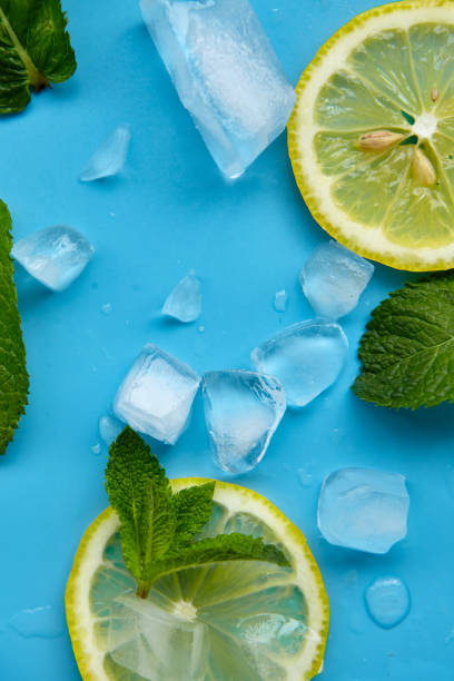 istock Composition with cut citrus fruits on blue background. Creative summer background composition with lemon slices, leaves mint and ice cubes. Minimal top down lemonade drink concept.Top view 1329378845