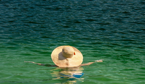 A bright wide-brimmed hat on a woman in clear emerald water.
